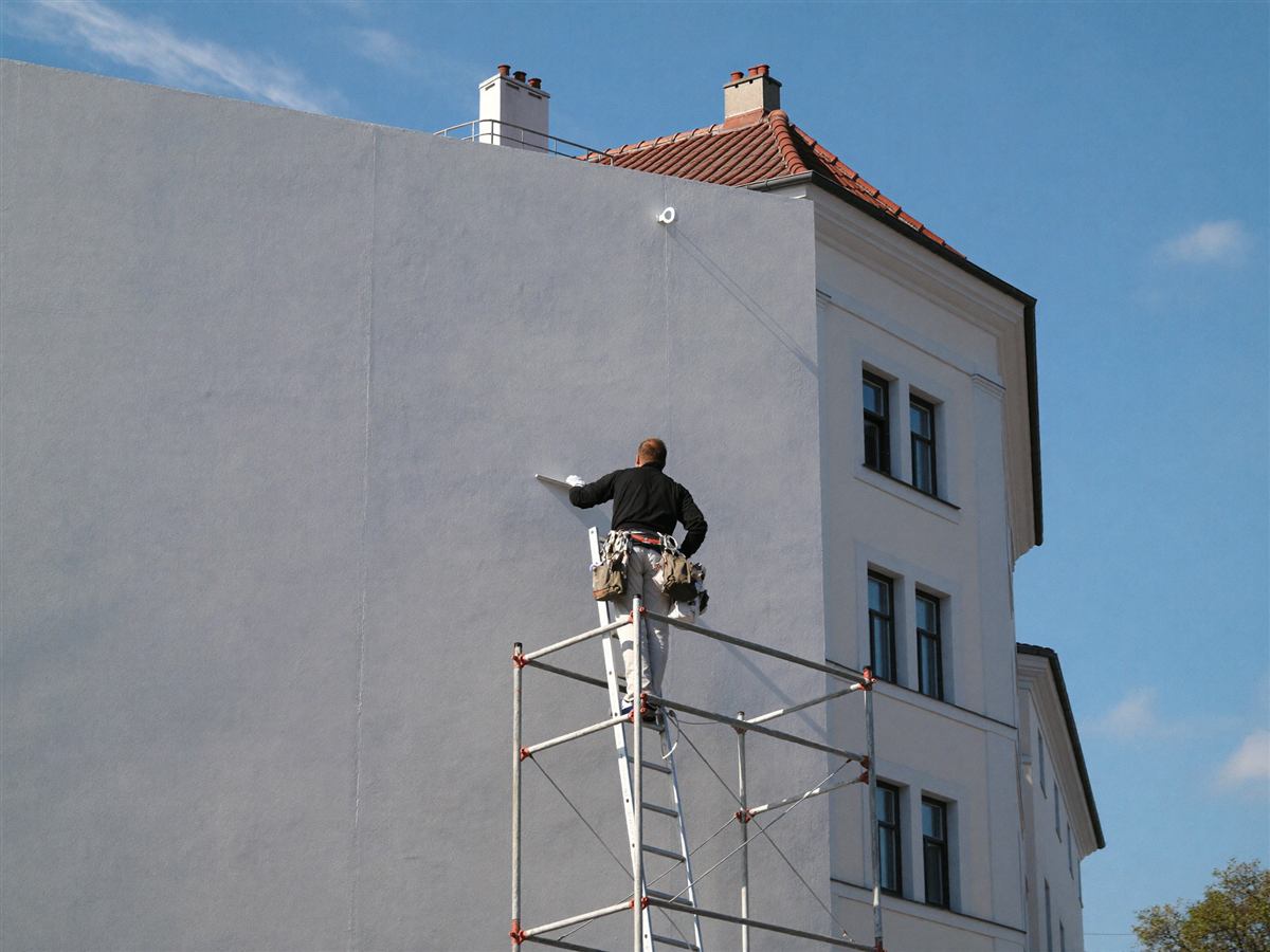 Fassadenmaler auf dem Gerüst streicht die Außenfassade eines Berliner Altbaus weiß